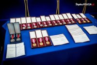 Stół nakryty niebieskim obrusem z przygotowanymi odznaczeniami  Za Długoletnią Służbę i Za Zasługi dla Policji