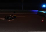 Zdjęcie kolorowe: noc, na pasie jezdni przewrócony żółty motor obok policyjnego radiowozu