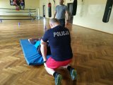 Zdjęcie kolorowe: dwóch zabrzańskich policjantów w strojach sportowych na sali gimnastycznej pod nadzorem policyjnego instruktora wykonują ćwiczenia podczas egzaminu sprawnościowego