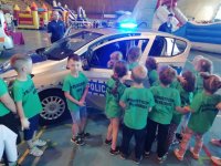 Zdjęcie kolorowe: zabrzański policjant na hali MOSiR z dziećmi przy radiowozie