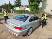 Zdjęcie kolorowe: policjant ruchu drogowego  i funkcjonariusz z Krajowej Administracji Skarbowej wraz z psem wyszkolonym do wyszukiwania narkotyków sprawdzają pojazd