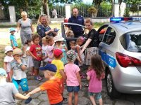 Zdjęcie kolorowe:  Policjant przy radiowozie wraz z  grupą dzieci.