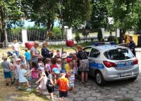 Zdjęcie kolorowe:  Policjant wraz  z  grupą dzieci  przy radiowozie policyjnym