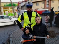 Zdjęcie kolorowe: policjant podczas akcji znicz 2019 rozdaje odblaski dzieciom