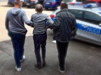 Zdjęcie kolorowe: policjanci, z którego zatrzymanym prowadzą do radiowozu