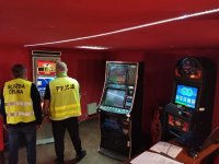 Zdjęcie kolorowe: policjant i funkcjonariusz KAS zabezpieczają nielegalne automaty do gier.